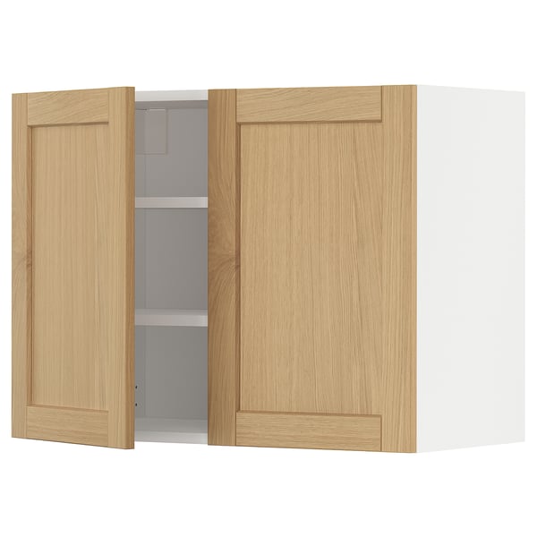 O armário de parede de cozinha METOD com portas de carvalho claro. Tem um design emoldurado com bordas chanfradas. Uma porta está aberta, revelando prateleiras internas.