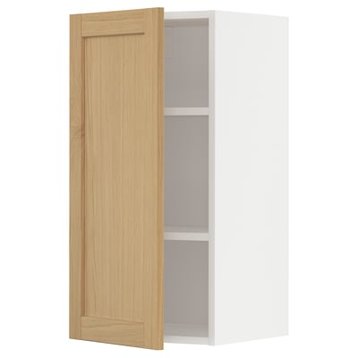 Apresenta um armário de parede de cozinha branco METOD com uma única porta de madeira aberta, com folheado de carvalho e extremidades biseladas.