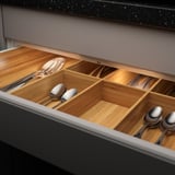 Organizador de gavetas de madeira com led embutido, iluminando utensílios de cozinha em compartimentos.