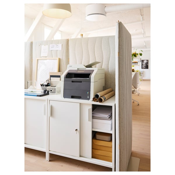 Espaço de escritório moderno com tela acústica cinza, impressora, mesa e decoração.