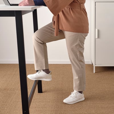 Uma pessoa se inclina em uma mesa de conferência alta com apoio para os pés, mostrando seu uso tanto para sentar quanto para ficar em pé.