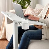 Pessoa sentada em um sofá usando uma mesa de laptop ajustável em altura com um porta-copos.