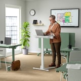 Um escritório com uma mesa para laptop ajustável em altura usada por uma pessoa, com um suporte de caneca móvel e rodízios para facilitar a mobilidade.