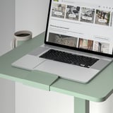 Laptop na mesa ajustável com xícara de café, exibindo o site de móveis de escritório.
