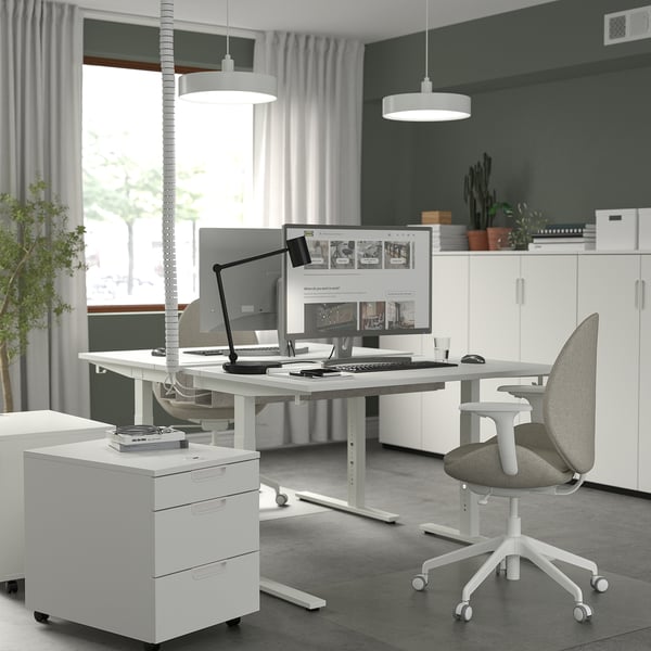 Escritório em casa moderno com mesa ajustável em altura, monitores duplos, cadeira de escritório e plantas.