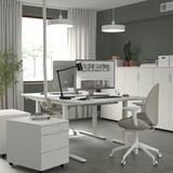 Escritório em casa moderno com mesa ajustável em altura, monitores duplos, cadeira de escritório e plantas.