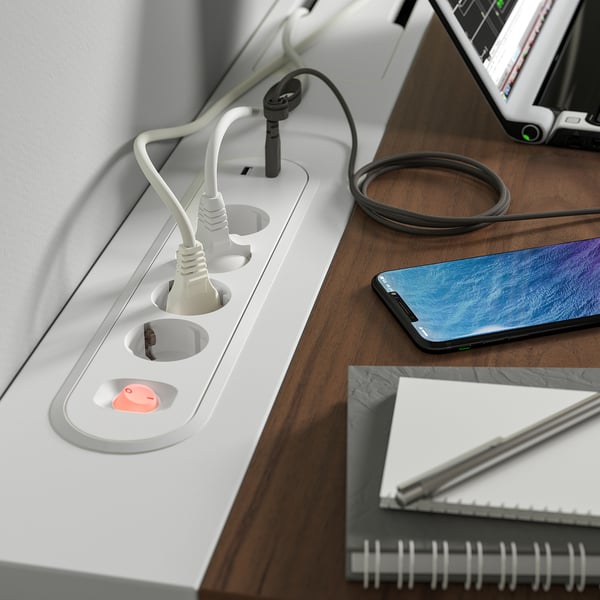 Uma mesa com tomadas embutidas e uma bandeja de gerenciamento de cabos. Um smartphone e um notebook são colocados sobre a mesa.