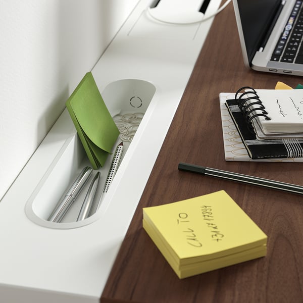 Mesa de madeira com organizador branco segurando canetas, notas adesivas e clipes. Laptop, caderno e notas adesivas amarelas estão sobre a mesa.