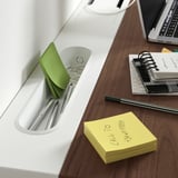 Mesa de madeira com organizador branco segurando canetas, notas adesivas e clipes. Laptop, caderno e notas adesivas amarelas estão sobre a mesa.