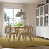 Sala de jantar moderna com mesa de madeira clara, cadeiras, luminária pendente cinza e tapete MORUM verde.