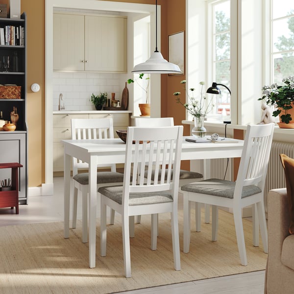 Uma mesa de jantar NÄSINGE branca com quatro cadeiras a condizer perto de uma cozinha, combinando estilos modernos e de quinta.