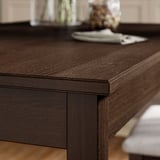 Mesa de jantar em madeira escura com superfície polida, bordas quadradas, grão visível, acabamento robusto e itens decorativos.