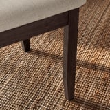 Grande plano da perna da cadeira NÄSINGE, madeira escura sobre tapete texturizado. Robusto e elegante, apresentando detalhes finos e construção de qualidade.