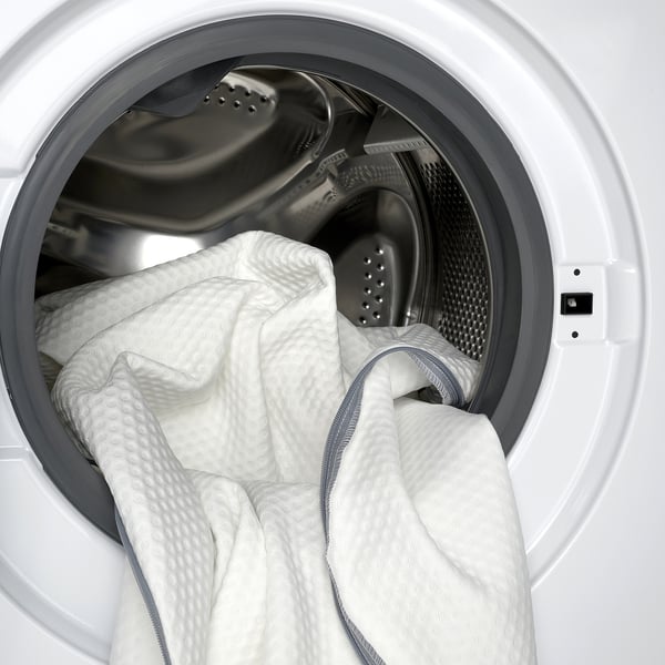 Máquina de lavar roupa com lençóis brancos, incluindo um colchão, indicando fácil cuidado e limpeza.