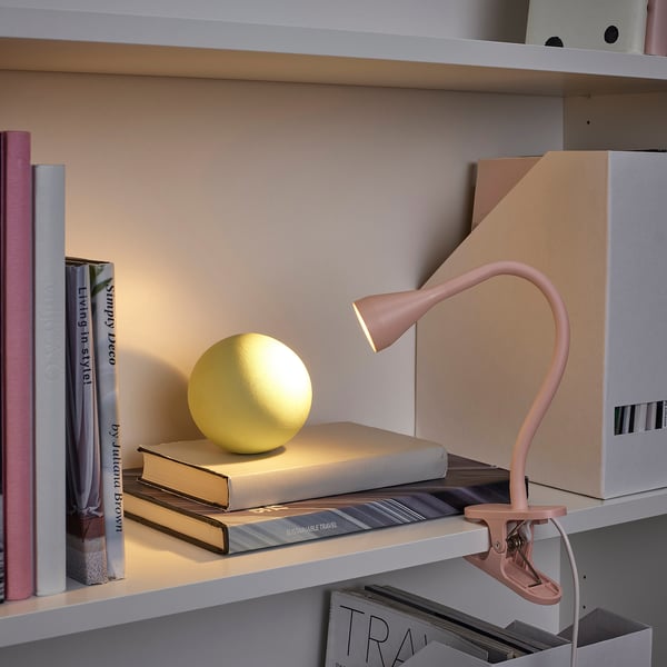Estante com candeeiro NÄVLINGE, que ilumina uma esfera amarela em livros empilhados.