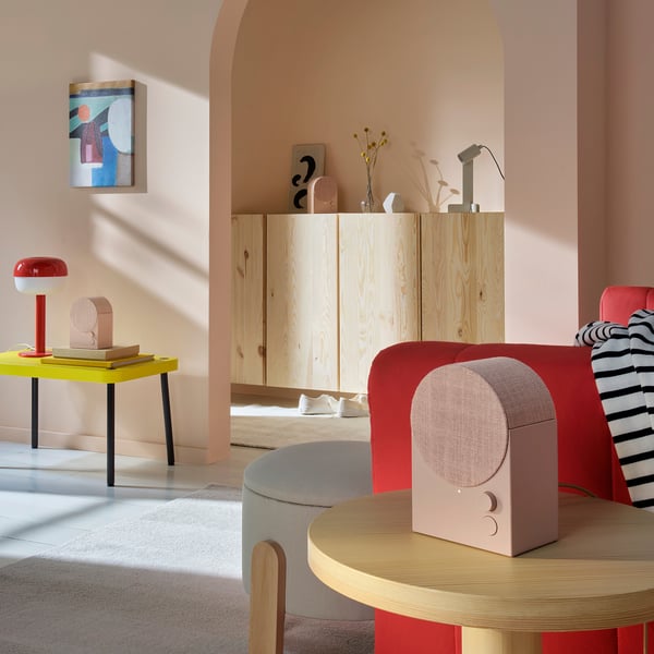 Sala de estar moderna com esquema de cores pastel. Um alto-falante vermelho curvo em uma mesa de madeira, ao lado de uma cadeira vermelha de pelúcia.