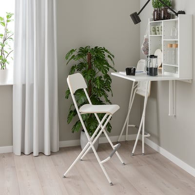 Mesa compacta minimalista e cadeira dobrável. Design branco e moderno, ideal para espaços pequenos. Cercado por plantas e armazenamento.