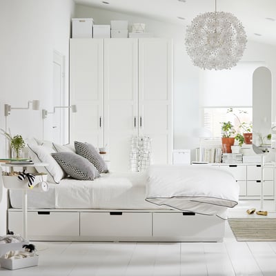 Quarto branco moderno com estrutura de cama NORDLI, detalhes em preto, luz suspensa, plantas e decoração minimalista.
