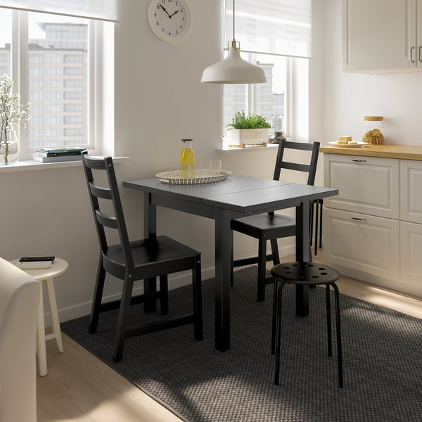 Conjunto de jantar pequeno NORDVIKEN preto na cozinha luminosa. Inclui mesa e cadeiras extensíveis, posicionadas perto de armários brancos.