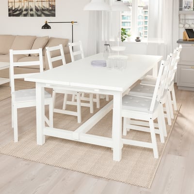 Pequeno conjunto de jantar branco com mesa extensível e 6 cadeiras em sala iluminada e aconchegante.