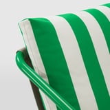 Uma almofada listrada verde e branca em uma cadeira moderna, destacando design de qualidade e conforto.