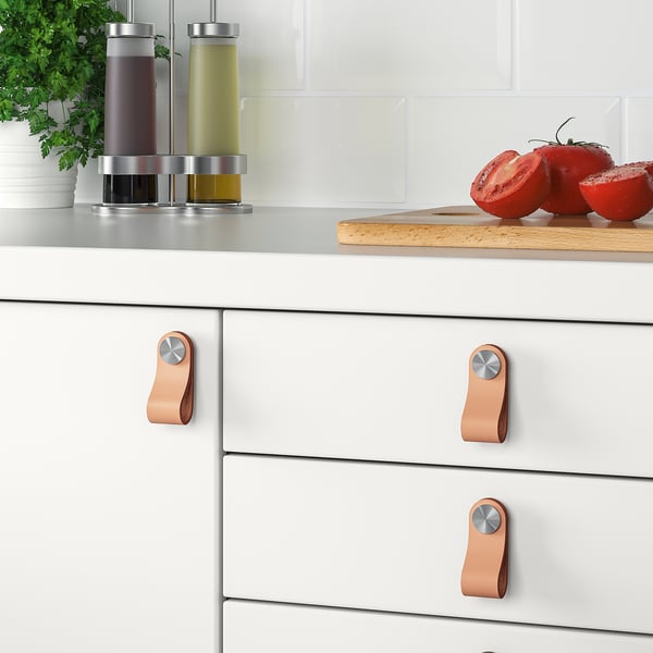 Móveis de cozinha modernos com puxadores em pele ÖSTERNÄS. Os puxadores se encaixam em portas de 16 a 21 mm de espessura. Parafusos incluídos. Tomates frescos e ervas no balcão.