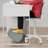 Pessoa sentada em uma mesa moderna, usando laptop e apoio para os pés ÖVNING para manter uma postura confortável e ereta.