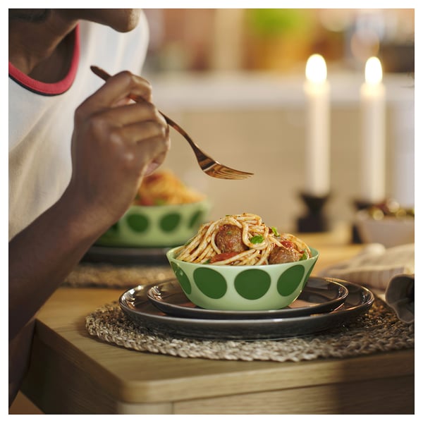 Uma pessoa comendo espaguete de uma tigela verde de bolinhas. Velas iluminam a mesa de madeira.