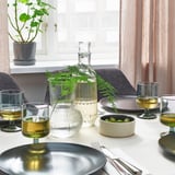 Configuração moderna da mesa de jantar com copos, pratos e vegetação minimalistas.