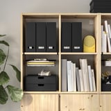 Prateleira de madeira moderna com pastas pretas, livros, alto-falante amarelo e planta. Armazenamento organizado com clipes e prateleiras ajustáveis.