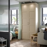Um quarto moderno com guarda-roupa PAX bege, sofá cinza e cortinas verdes, com cama e varanda.