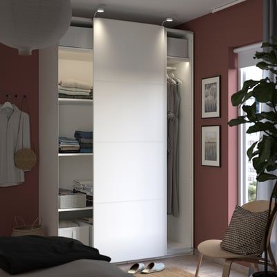 Quarto moderno com guarda-roupa PAX branco, portas espelhadas e sólidas, roupas e arte.