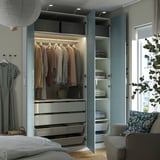 Quarto com roupeiro PAX com roupa, gavetas e prateleiras. Inclui espaço para pendurar, gavetas e cestos de armazenamento, iluminados por iluminação integrada.