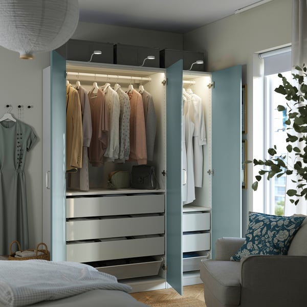 Guarda-roupa azul aberto com armazenamento de roupas iluminado, gavetas e espaço para pendurar em um quarto aconchegante.