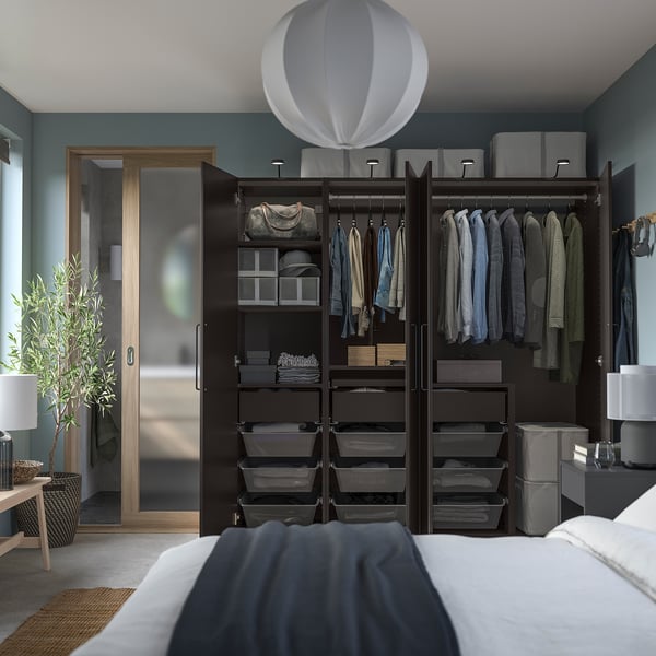 Quarto moderno com paredes azuis, guarda-roupa PAX preto, roupas e iluminação suave.