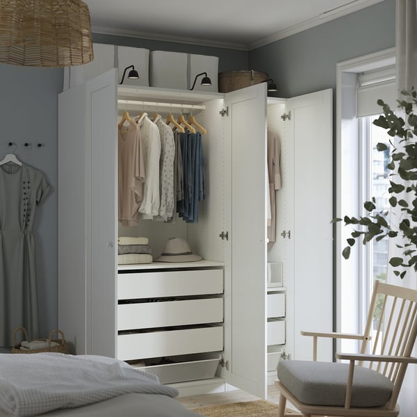 Quarto com guarda-roupa branco aberto exibindo roupas, gavetas e caixas de armazenamento. Cesta e chapéu em cima, cabides iluminados.