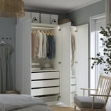 Quarto com guarda-roupa branco aberto exibindo roupas, gavetas e caixas de armazenamento. Cesta e chapéu em cima, cabides iluminados.