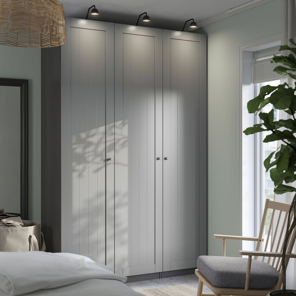 Quarto moderno com guarda-roupas ikea PAX elegantes, luzes, cadeira e planta.