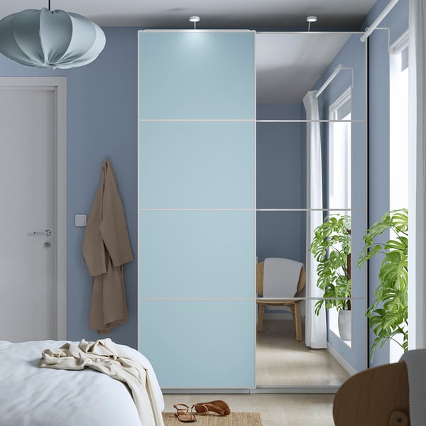 Quarto moderno com guarda-roupa PAX azul, portas de correr de vidro, plantas e cama branca.