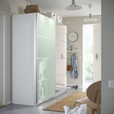 Entrada moderna com grande guarda-roupa PAX branco, portas de vidro fosco, tapete de juta, jaqueta azul e relógio de parede, bem iluminado por luz natural.