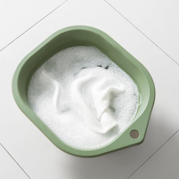 Banheira verde dobrável com roupas brancas, ideal para lavar as mãos e limpar esfregonas.