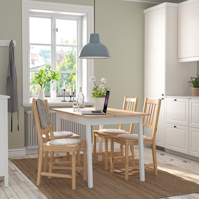 Conjunto de jantar com mesa quadrada, quatro cadeiras almofadadas, laptop e decoração.