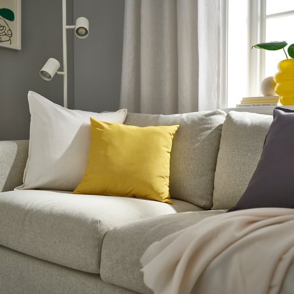 Almofada quadrada PROFETBLOMMA amarela em sofá cinza, com padrão sutil, outras almofadas, manta bege.