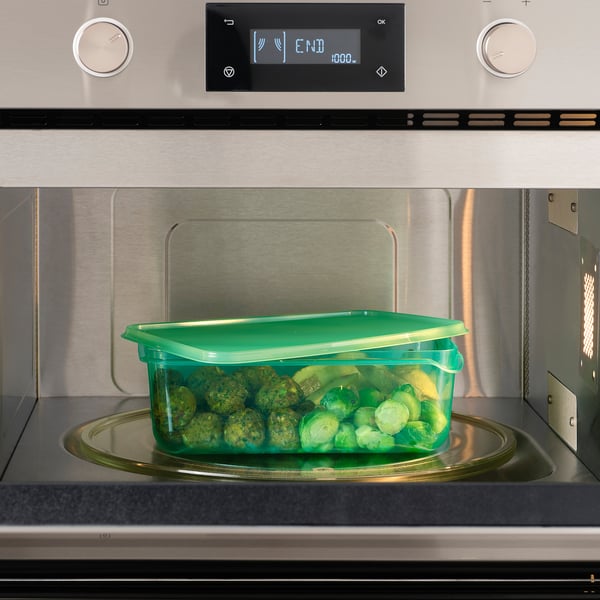 Recipiente de brócolis no microondas, aquecido com segurança em um recipiente transparente para alimentos verdes com tampa.