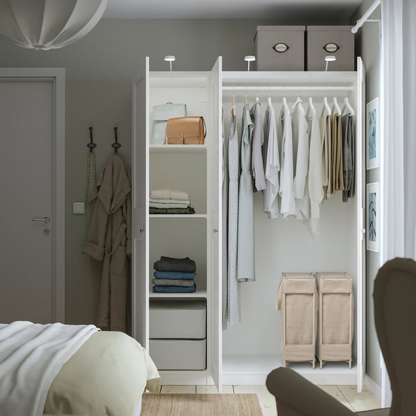 Quarto organizado com roupeiro a exibir roupas, toalhas e uma mala bege. Um cesto estreito de roupa suja chamado PURRPINGLA utiliza eficientemente o espaço vertical.