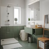 Banheiro moderno com azulejos verdes, banheira branca, chuveiro de vidro e prateleira de bambu com cadeira e toalheiro combinados.