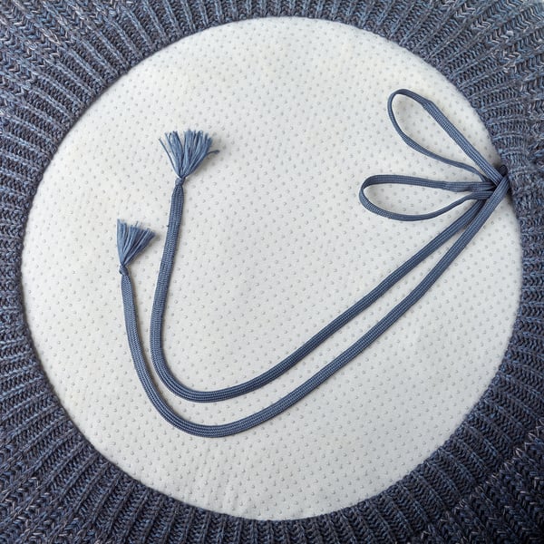 Pouffe azul com capa de malha, com borlas e cordões para apelo estético e funcional.