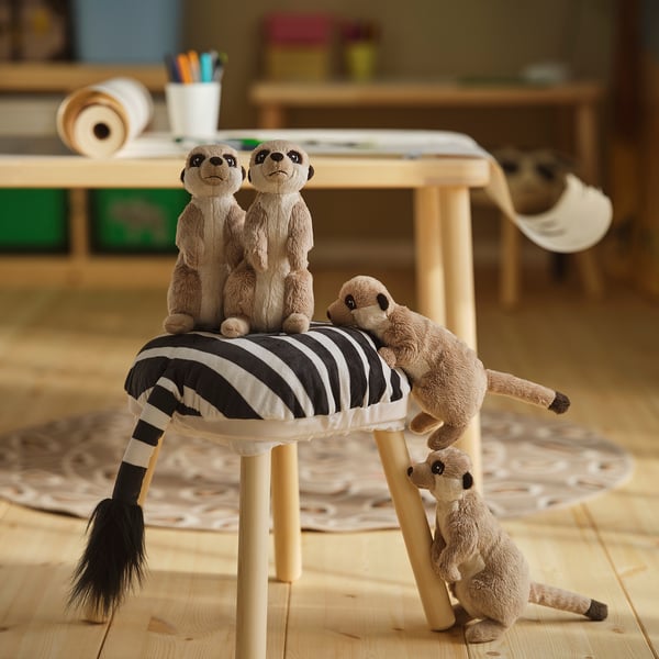 Meerkat bichos de pelúcia em um banquinho; dois sentados, um em pé, um deitado. Quarto infantil com piso e mesa de madeira.