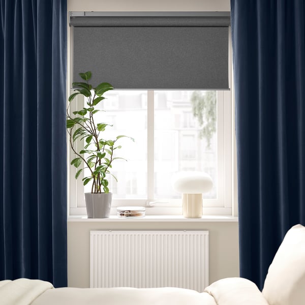 Quarto moderno com cortinas de veludo azul, planta, luminária branca.