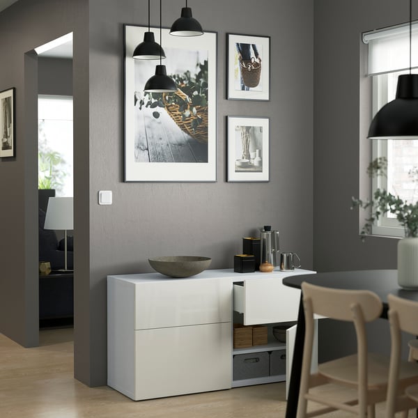 Sala de jantar moderna com armário branco, lâmpadas pretas, quadros emoldurados e plantas.